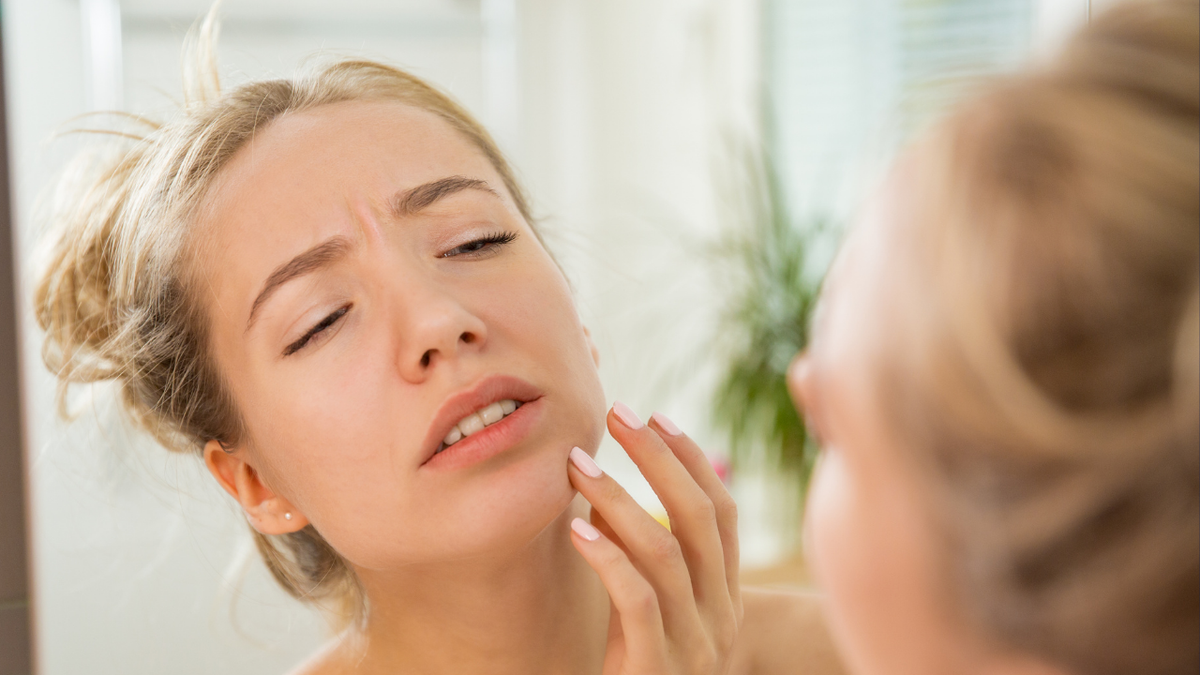 Tired Skin - A concerned woman examining her chin in the mirror, illustrating skincare challenges related to tired and stressed skin.